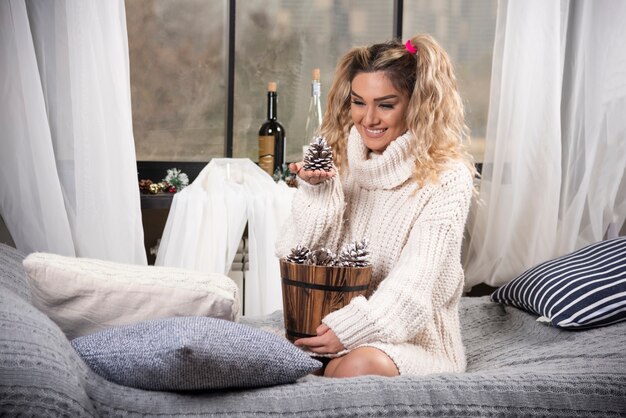 Mujer rubia en sudadera blanca mirando piñas.