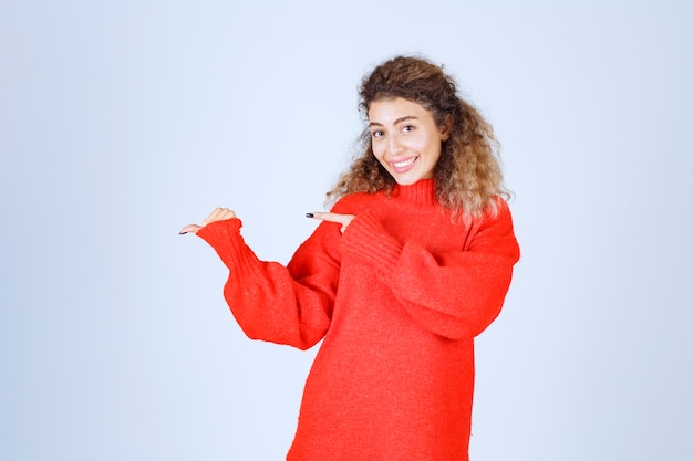 Mujer rubia con sudadera roja apuntando en algún lugar del lado izquierdo.