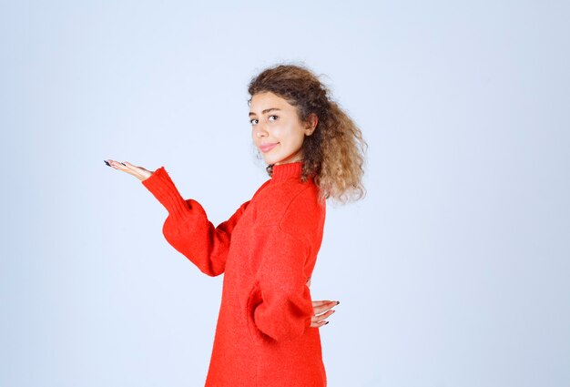 Mujer rubia con sudadera roja apuntando en algún lugar del lado izquierdo.