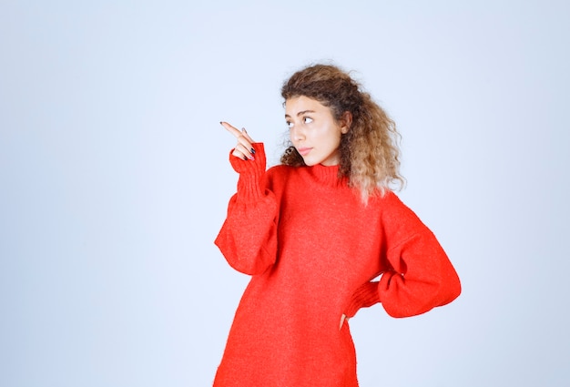 Foto gratuita mujer rubia con sudadera roja apuntando en algún lugar del lado izquierdo.