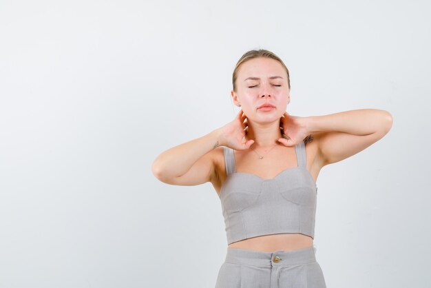 La mujer rubia sueña sosteniendo sus manos detrás del cuello en un fondo blanco