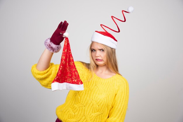 Mujer rubia en suéter amarillo mirando el sombrero de Santa con asco.