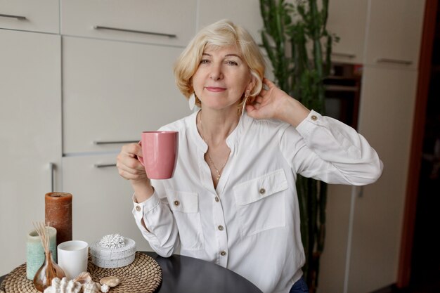 Mujer rubia con taza de té y sentado en la cocina moderna