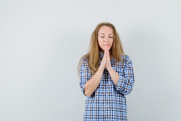 Mujer rubia tomados de la mano en gesto de oración en camisa y mirando esperanzado,