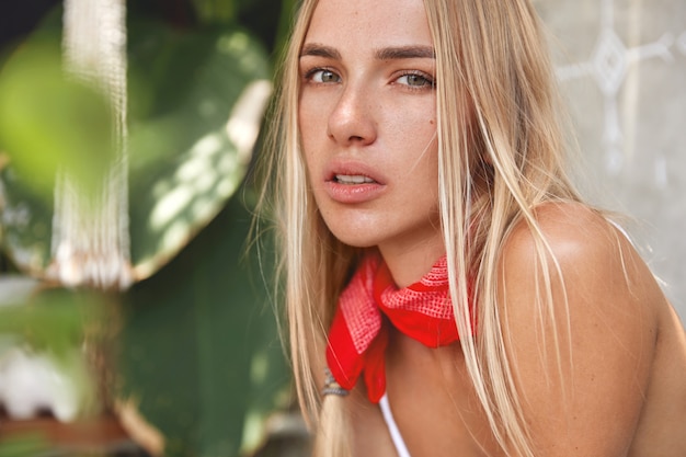 Mujer rubia con top blanco y pañuelo rojo posando en un café