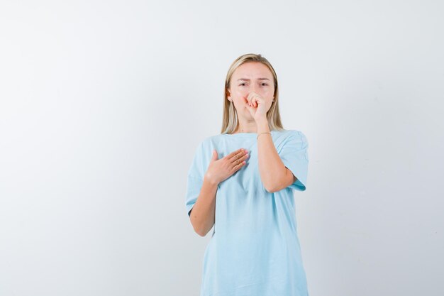 Mujer rubia tosiendo, sosteniendo el puño en la boca en camiseta azul y mirando agotado