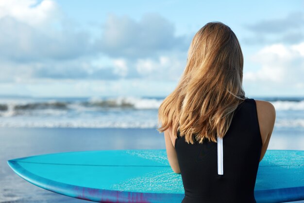Mujer rubia en traje de baño con tabla de surf en la playa