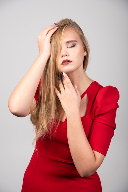 Mujer rubia en traje rojo sosteniendo su cabello.