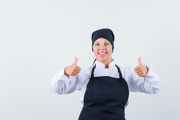 Mujer rubia en uniforme de cocinero negro mostrando doble pulgar hacia arriba y luciendo bonita