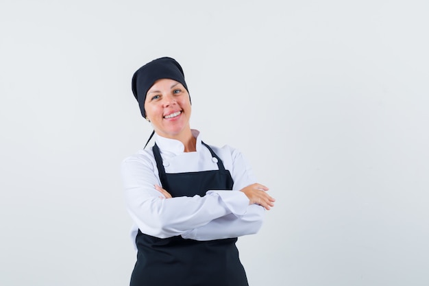 Mujer rubia en uniforme de cocinero negro de pie con los brazos cruzados y mirando bastante