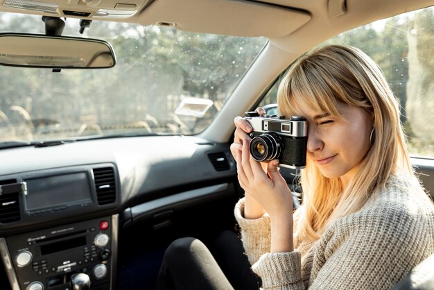 Mujer rubia usando una cámara vintage en coche