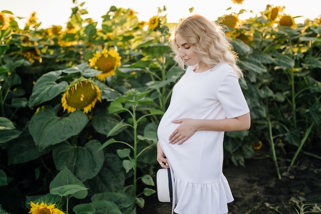 Una mujer rubia con un vestido blanco en el campo con girasoles