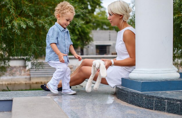 Una mujer rubia con vestido blanco y su pequeño y lindo hijo.