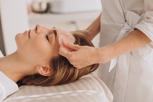 Mujer en el salón haciendo tratamientos de belleza con piedra gua sha