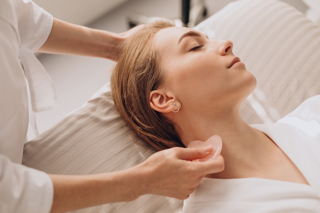 Mujer en el salón haciendo tratamientos de belleza con piedra gua sha