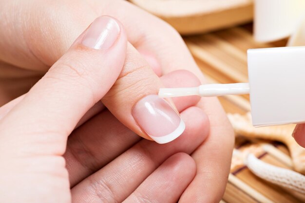 Mujer en un salón de uñas recibiendo manicura. Esteticista aplicando esmalte de uñas en una miniatura.