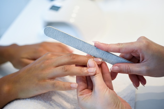 Mujer en un salón de uñas recibiendo una manicura con una lima de uñas