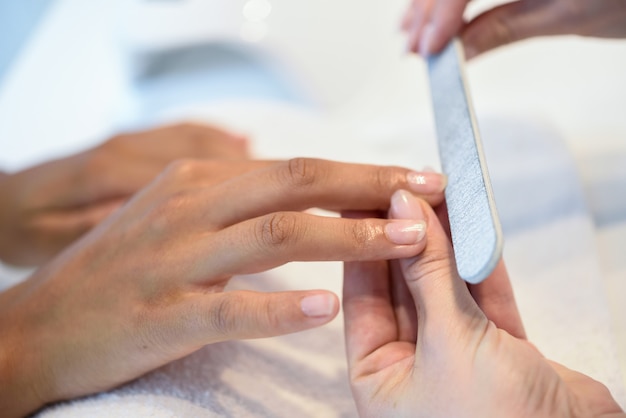 Mujer en un salón de uñas recibiendo una manicura con una lima de uñas