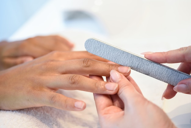 Mujer en un salón de uñas recibiendo una manicura con una lima de uñas