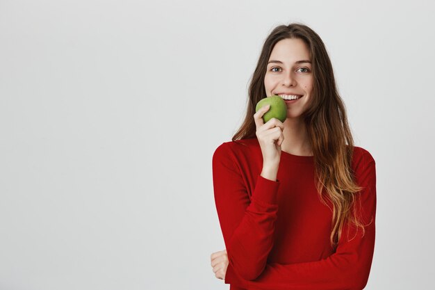 Mujer sana atractiva sonriente que come la manzana verde