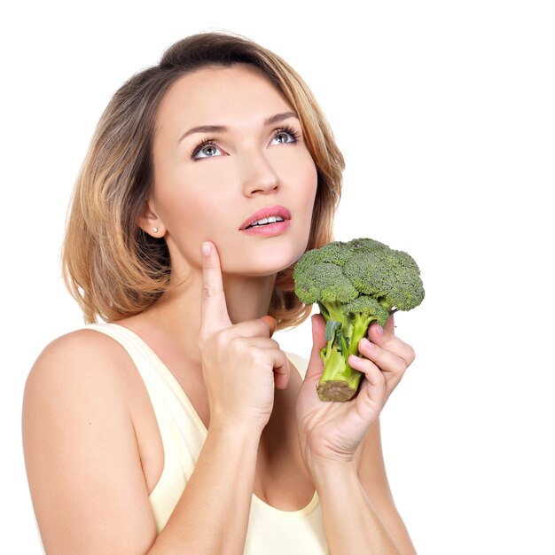 La mujer sana joven hermosa sostiene el brócoli - aislado en blanco.