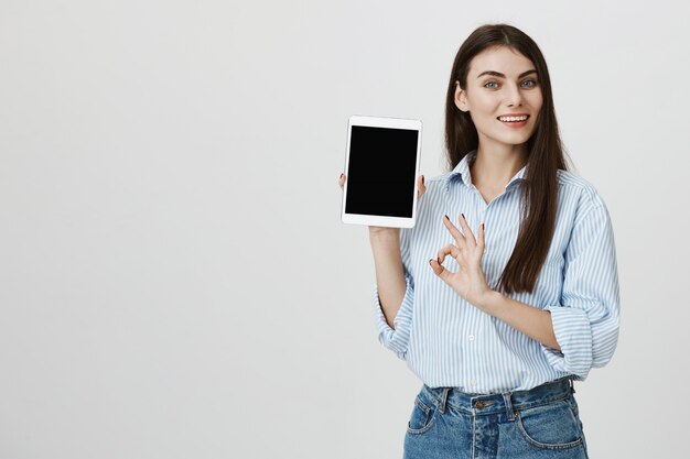 Mujer satisfecha mostrando tableta digital y signo bien