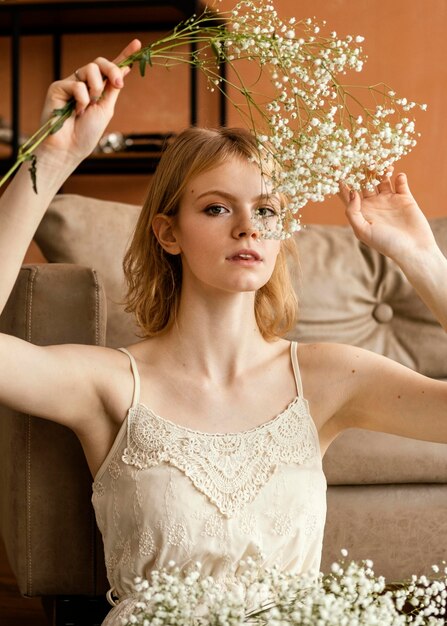 Mujer seductora posando junto al sofá mientras sostiene delicadas flores de primavera