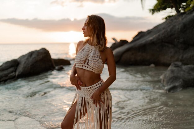 Mujer seductora con vestido de ganchillo boho blanco posando en la playa. Foto de moda de verano y vacaciones tropicales.