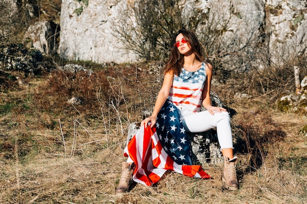 Foto gratuita mujer segura con la bandera de estados unidos sentado en piedra