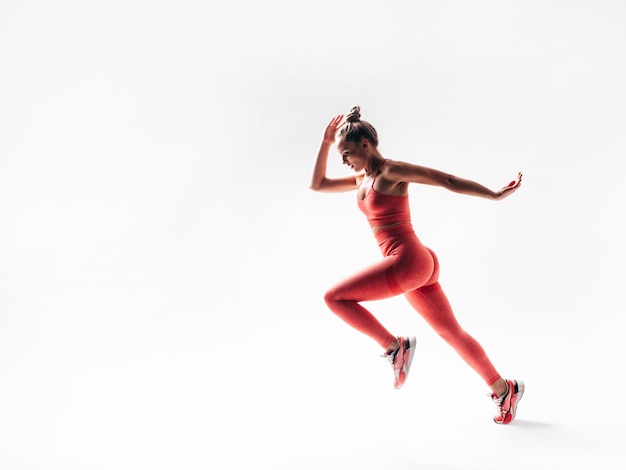 Mujer segura de fitness en ropa deportiva rosa Modelo hermoso joven con cuerpo perfecto Mujer aislada en blanco en el estudio Alegre y feliz Saltando y corriendo