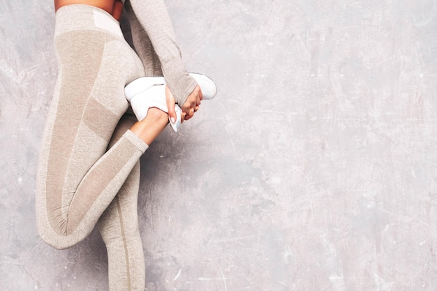 Mujer segura de fitness en ropa deportiva Sexy modelo hermosa joven con cuerpo perfecto Mujer posando cerca de la pared gris en el estudio Estirándose antes de entrenar