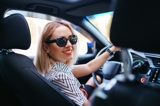 Mujer segura y hermosa en gafas de sol. Vista trasera de la atractiva mujer joven en ropa casual conduciendo un coche