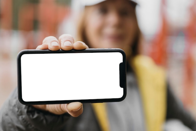 Mujer senior Defocused sosteniendo smartphone al aire libre