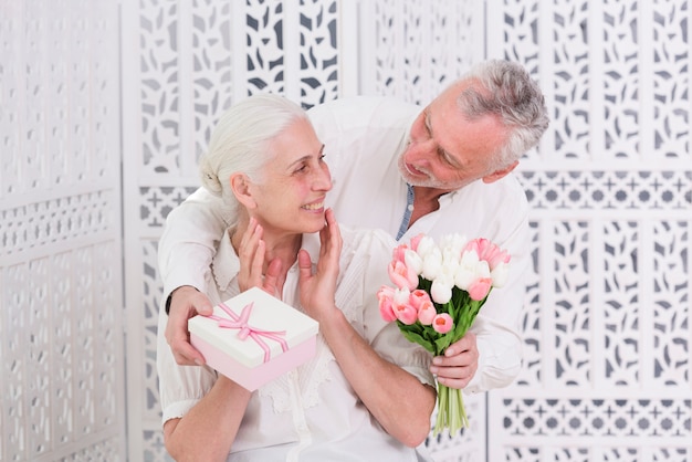 Mujer senior feliz recibiendo un regalo sorprendido de su amoroso esposo