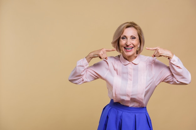 Mujer senior sonriente apuntando a sí misma