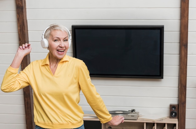 Mujer senior sonriente escuchando música a través de auriculares inalámbricos