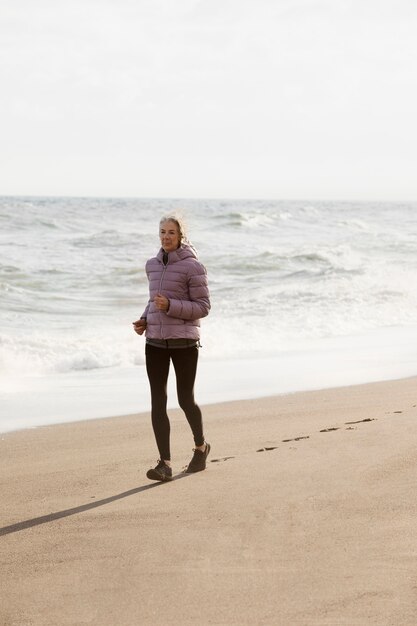 Mujer senior de tiro completo corriendo en la playa