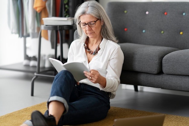 Mujer senior de tiro completo leyendo en el piso