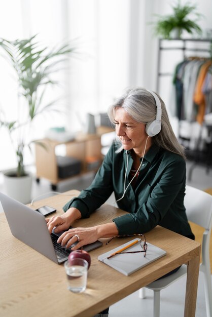 Mujer senior de tiro medio con auriculares en el escritorio