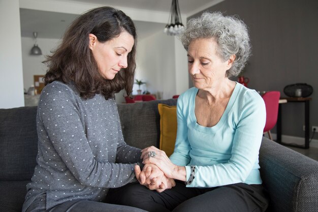 Mujer senior tranquila y su hija sentada y tomados de la mano