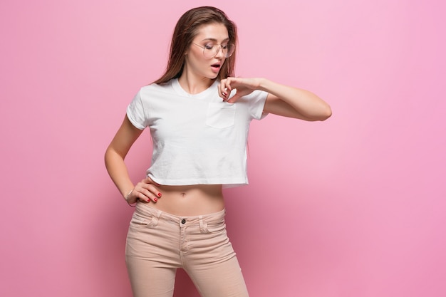 Mujer sensual bastante joven que presenta en la pared rosada vestida con jeans estilo hipster