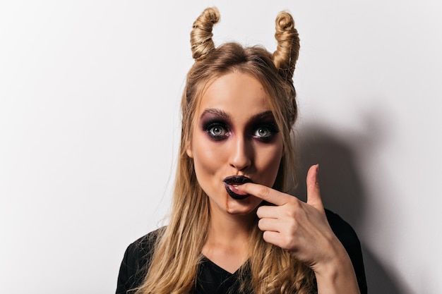 Foto gratuita mujer sensual con maquillaje negro posando en la fiesta de halloween. magnífica bruja con cabello rubio disfrutando de la sesión de fotos.