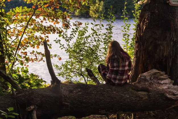 Mujer sentada en el árbol disfrutando de la vista con un mar