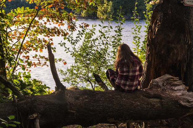 Mujer sentada en el árbol disfrutando de la vista con un mar