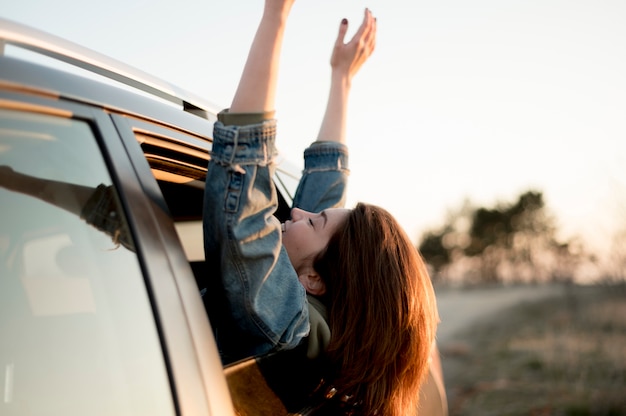 Mujer sentada en un automóvil con las manos y la cabeza al aire libre