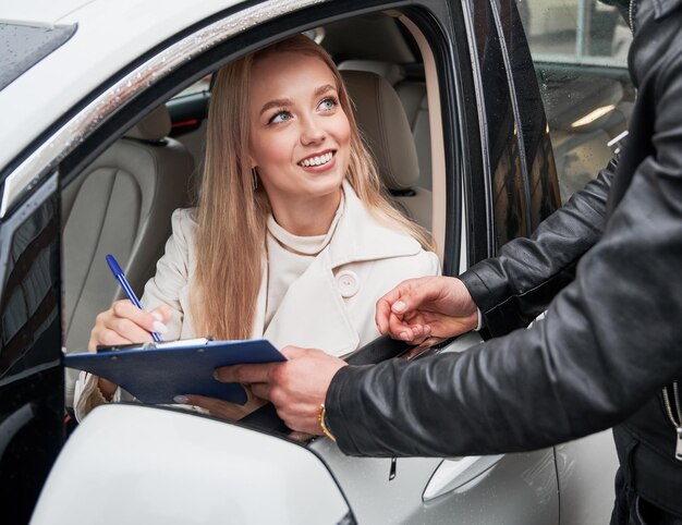 Mujer sentada en un automóvil nuevo y firmando un contrato de compra