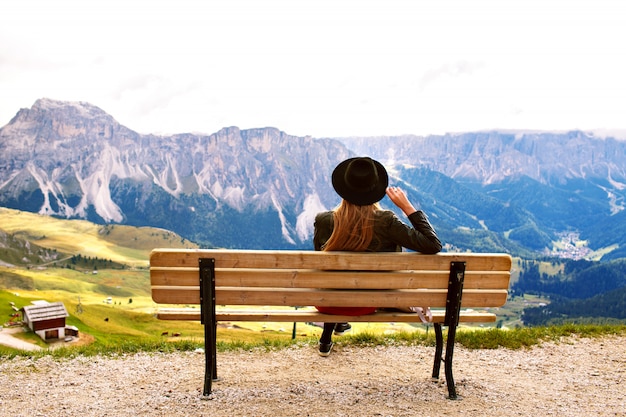 Mujer sentada en el banco final disfrutando de la vista sobre las enormes montañas Dolomitas italianas