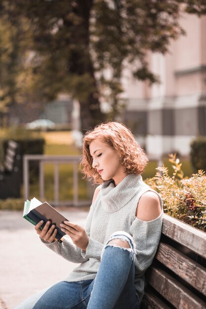 Mujer sentada en el banco y recitando volumen en el parque