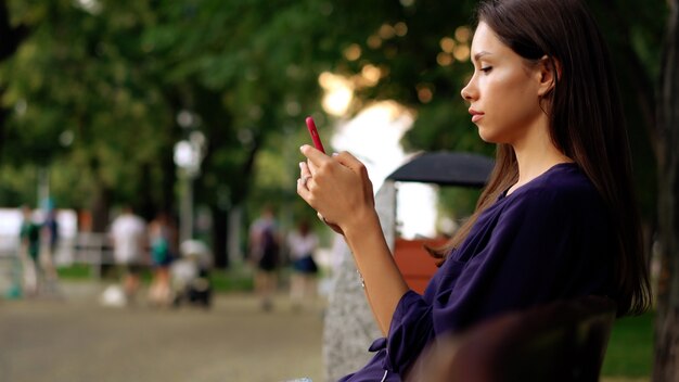 Mujer sentada en el banquillo y con smartphone. Vista cercana