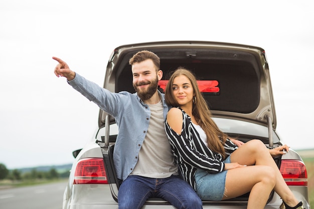 Mujer sentada en el baúl del auto mirando a su novio señalando